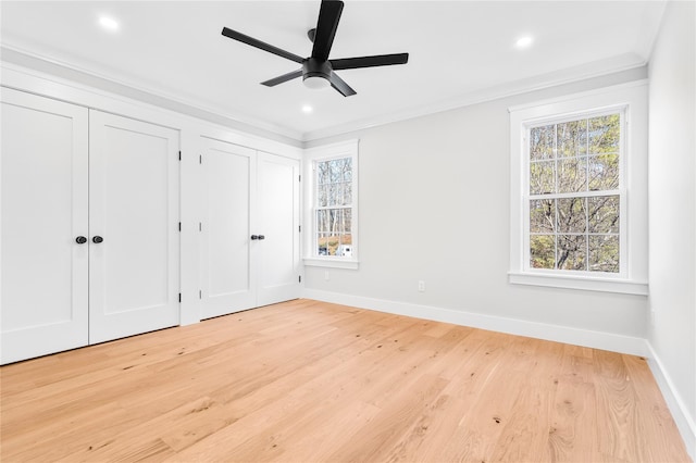 unfurnished bedroom with light wood-style floors, multiple windows, crown molding, and multiple closets