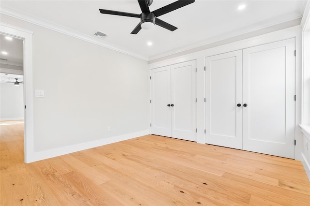 unfurnished bedroom featuring baseboards, light wood finished floors, visible vents, crown molding, and two closets