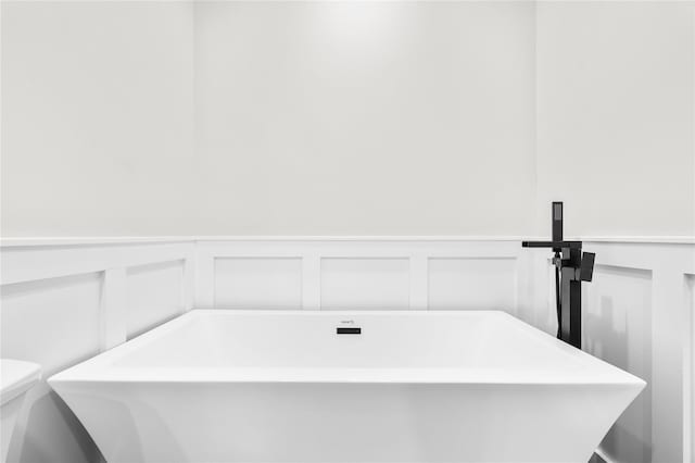 bathroom with a soaking tub, a wainscoted wall, toilet, and a decorative wall