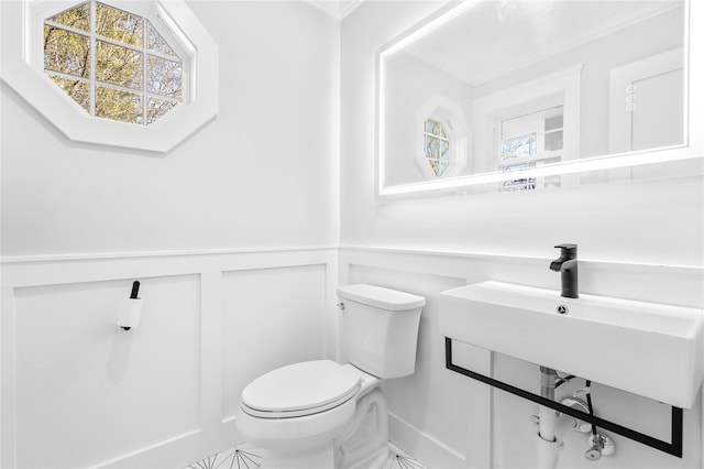 half bath featuring a decorative wall, wainscoting, and toilet