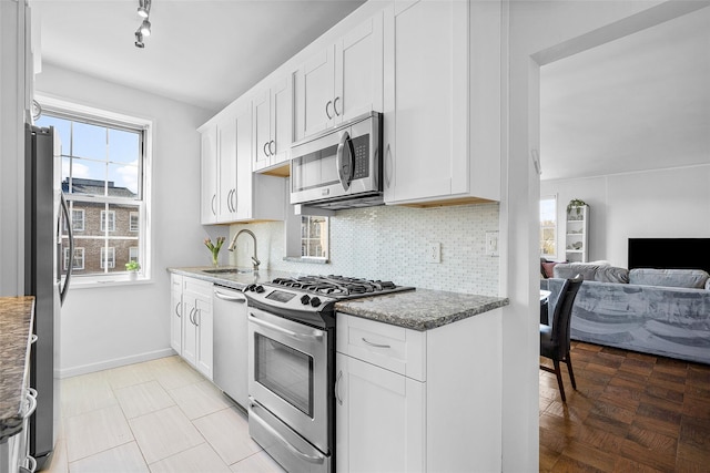 kitchen featuring appliances with stainless steel finishes, open floor plan, a sink, white cabinetry, and backsplash