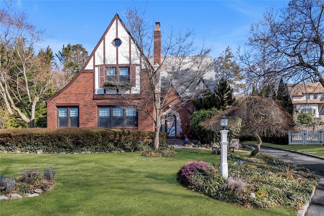 tudor-style house featuring a chimney, a front lawn, and brick siding