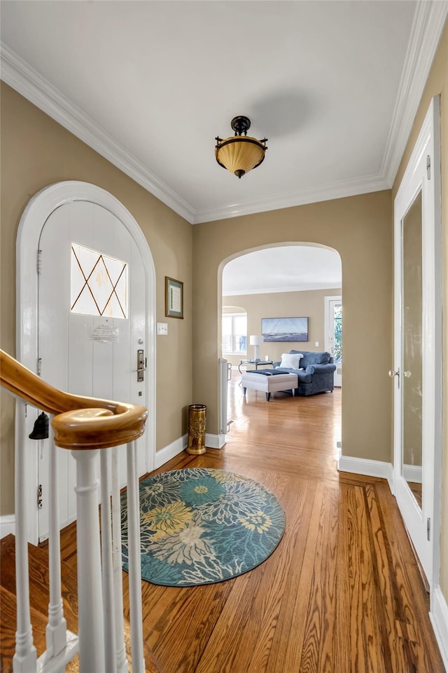 foyer entrance with a healthy amount of sunlight, arched walkways, wood finished floors, and ornamental molding