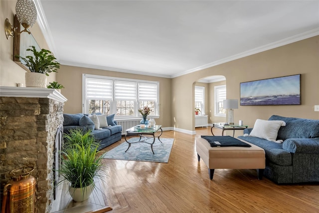 living area featuring arched walkways, ornamental molding, baseboards, and light wood-style floors