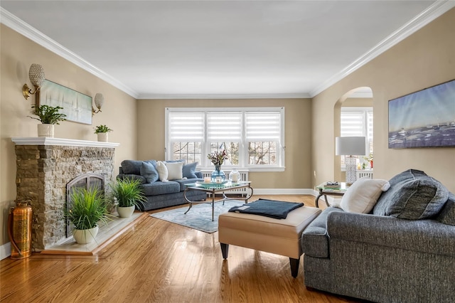 living area featuring arched walkways, ornamental molding, a stone fireplace, wood finished floors, and baseboards