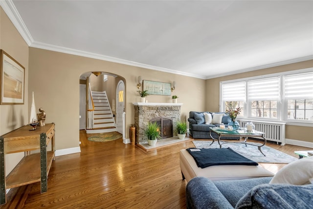 living area featuring arched walkways, crown molding, a fireplace with raised hearth, radiator heating unit, and wood finished floors