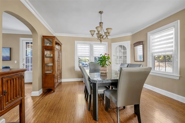 dining room with a healthy amount of sunlight, light wood-type flooring, arched walkways, and ornamental molding