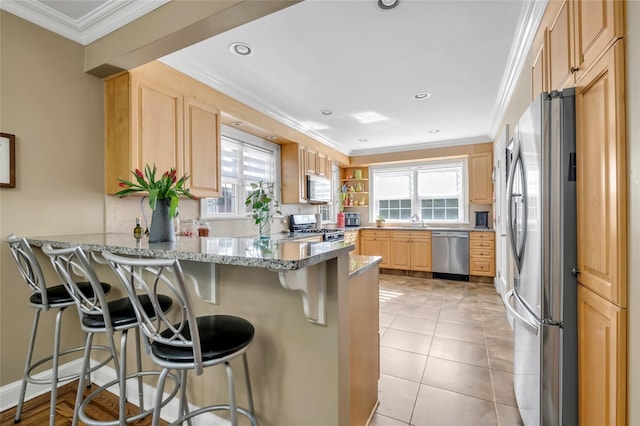 kitchen featuring crown molding, light brown cabinetry, appliances with stainless steel finishes, a peninsula, and a kitchen bar