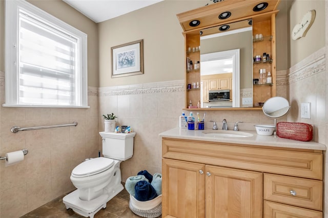 bathroom featuring a wainscoted wall, vanity, toilet, and tile walls