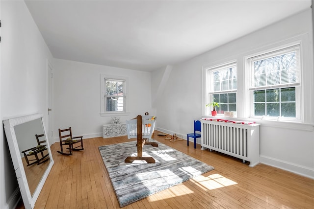 game room with baseboards, radiator heating unit, and light wood-style floors