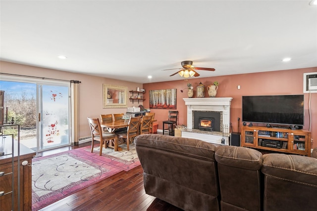 living area with dark wood finished floors, a ceiling fan, a baseboard radiator, a lit fireplace, and recessed lighting