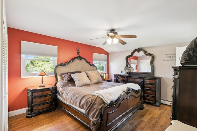 bedroom featuring multiple windows, baseboard heating, wood finished floors, and a ceiling fan