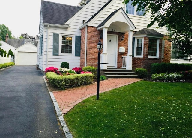 bungalow-style home with brick siding, a detached garage, a front lawn, and an outbuilding