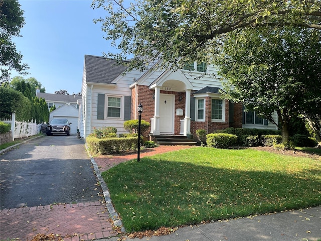 view of front facade with an outbuilding, roof with shingles, brick siding, a front yard, and fence