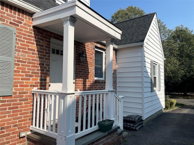 entrance to property featuring a shingled roof and brick siding