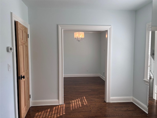 corridor featuring a notable chandelier, dark wood finished floors, and baseboards