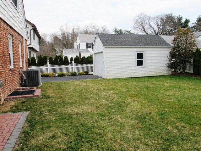 view of yard with a garage, an outbuilding, central AC, and fence