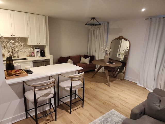 kitchen with white cabinets, light countertops, stainless steel dishwasher, light wood finished floors, and a kitchen bar