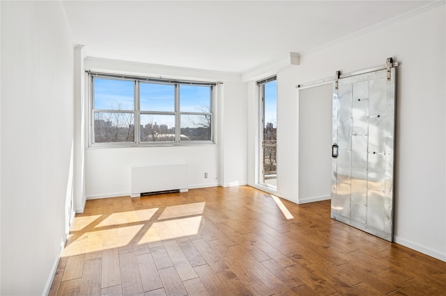 unfurnished room with a barn door, wood finished floors, baseboards, radiator, and crown molding