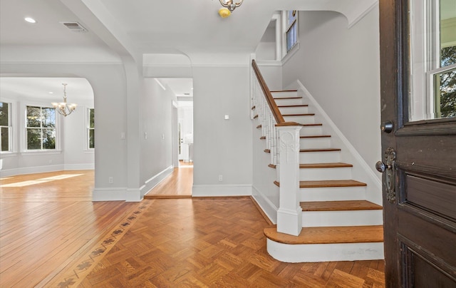 foyer featuring arched walkways, visible vents, baseboards, stairway, and an inviting chandelier