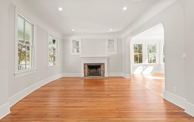 unfurnished living room with baseboards, arched walkways, light wood-type flooring, a fireplace, and recessed lighting