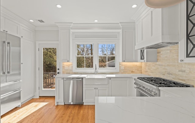 kitchen featuring visible vents, white cabinets, premium appliances, light stone counters, and a sink