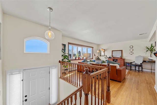 hallway with visible vents, light wood finished floors, and an upstairs landing