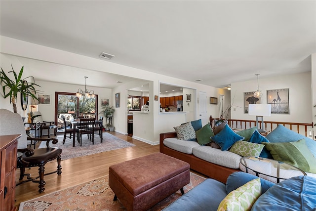 living area featuring baseboards, visible vents, light wood finished floors, and an inviting chandelier