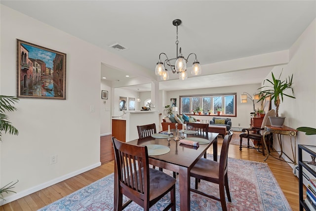 dining area featuring a chandelier, light wood-type flooring, visible vents, and baseboards