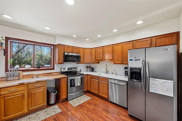 kitchen featuring recessed lighting, light countertops, appliances with stainless steel finishes, brown cabinetry, and dark wood finished floors