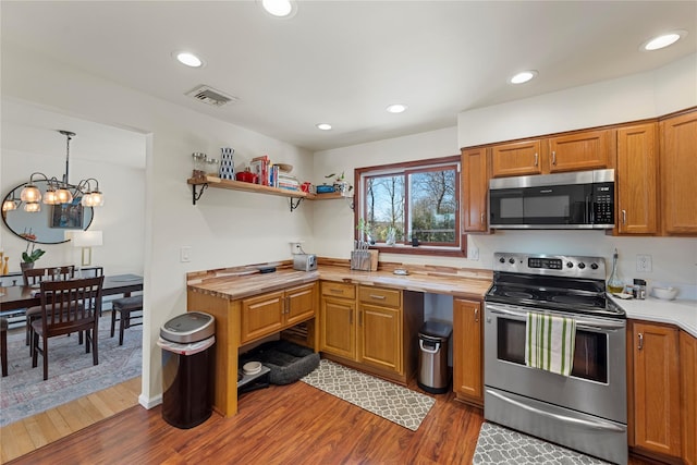 kitchen featuring hanging light fixtures, appliances with stainless steel finishes, brown cabinetry, and butcher block counters