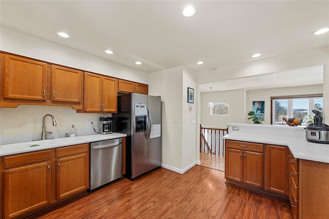 kitchen featuring brown cabinets, wood finished floors, stainless steel appliances, light countertops, and a sink