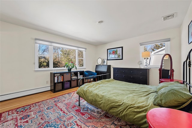 bedroom with a baseboard heating unit, light wood-type flooring, and visible vents