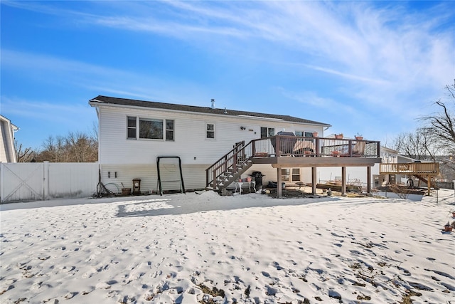 snow covered house with fence, stairway, and a wooden deck