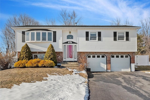 raised ranch featuring a garage, driveway, and brick siding