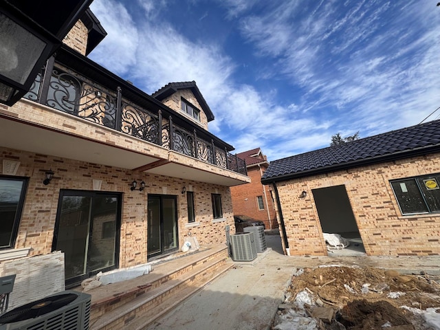 rear view of property featuring a tiled roof, brick siding, a balcony, and central AC unit