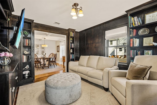 living area with beam ceiling, visible vents, light wood-style flooring, an inviting chandelier, and coffered ceiling