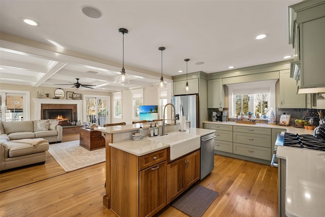 kitchen with stainless steel appliances, light countertops, a brick fireplace, a sink, and light wood-type flooring