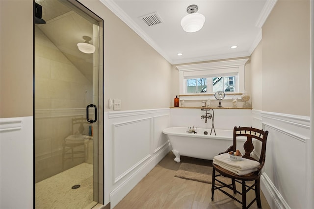 bathroom with visible vents, a wainscoted wall, crown molding, a freestanding bath, and a shower stall