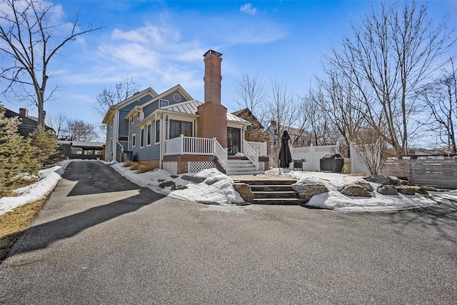 view of front facade with metal roof, fence, driveway, a standing seam roof, and a chimney