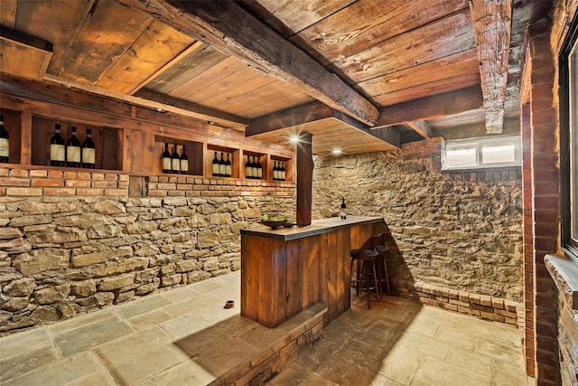 wine room with beam ceiling, stone tile flooring, bar area, and wood ceiling