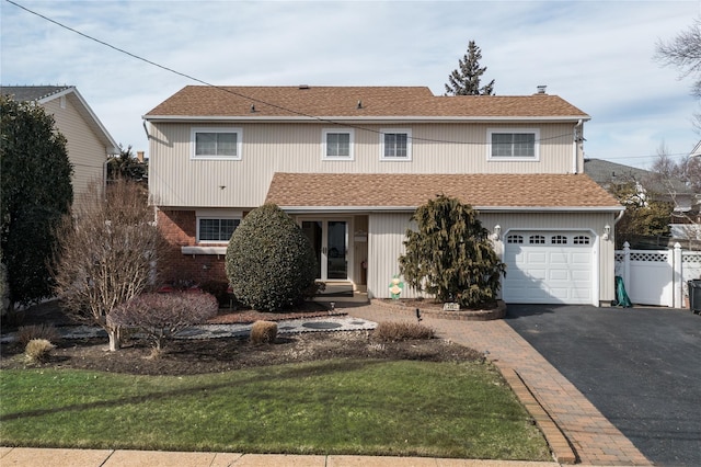 traditional-style home featuring aphalt driveway, a garage, brick siding, fence, and roof with shingles