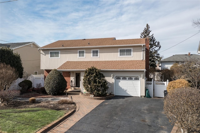 traditional home featuring a garage, a shingled roof, fence, and aphalt driveway