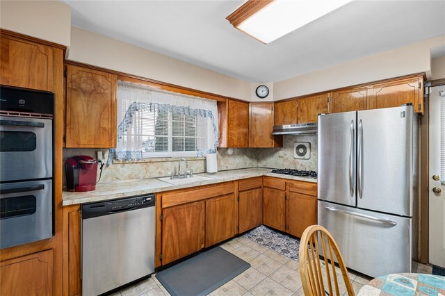 kitchen with stainless steel appliances, brown cabinetry, light countertops, and under cabinet range hood