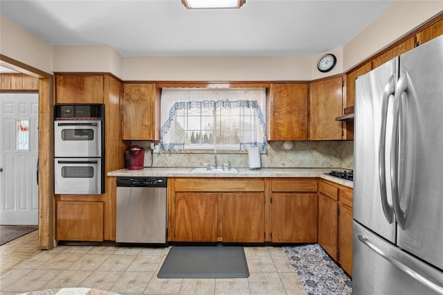 kitchen with stainless steel appliances, light countertops, brown cabinetry, a sink, and under cabinet range hood