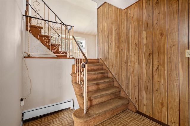 staircase featuring wood walls and a baseboard radiator