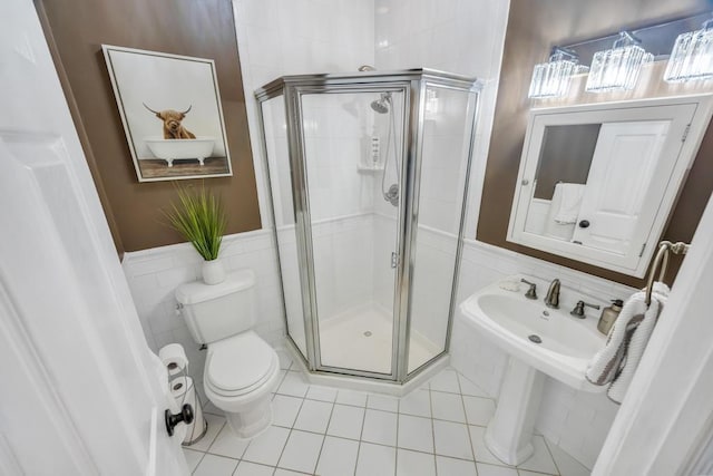 bathroom with toilet, a wainscoted wall, tile patterned floors, a shower stall, and tile walls