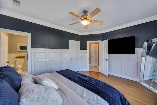 bedroom with wainscoting, visible vents, crown molding, and light wood finished floors