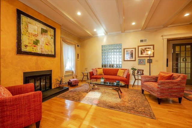 living area with beam ceiling, visible vents, ornamental molding, a glass covered fireplace, and wood finished floors