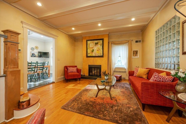living area featuring a fireplace, wood finished floors, visible vents, ornamental molding, and radiator heating unit